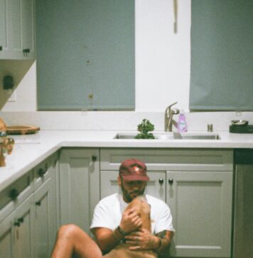 The Ultimate Puppy Training Schedule (8–16 Weeks Guide) Young man sitting on kitchen floor, gently holding a happy puppy in natural morning light.